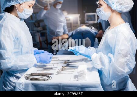 Nurse s hands holding surgical instruments and tools, close up including scalpels, forceps and tweezers arranged on a table. Surgeons at work in opera Stock Photo