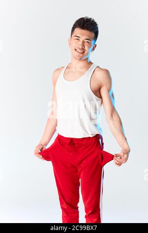 Young sporty stylish male dancer in red sweatpants posing isolated in studio over white background. Asian hipster bboy smiling at camera before traini Stock Photo