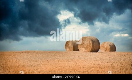 Three round bales, on the horizon, against a stormy sky.