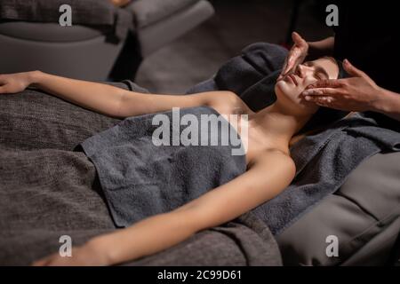 attractive caucasian lady get face lift massage, healthy skin without wrinkles, skin care concept. cropped masseur carefully do procedure Stock Photo