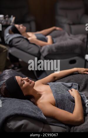 young and beautiful woman enjoy spending time in wellbeing salon, attractive lady lie on desk for massage with closed eyes before massage, other clien
