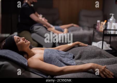 side view on young caucasian women relaxing in spa wellbeing salon, attractive ladies want to get rid of wrinkles. woman lie with closed eyes while ma Stock Photo