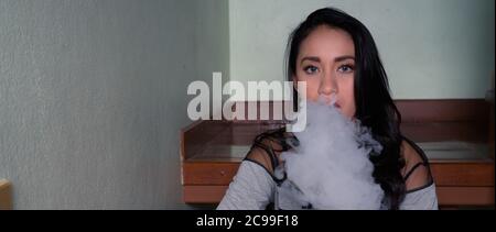 Young beautiful Asian woman vaping at home Stock Photo