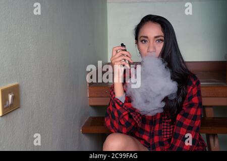 Young beautiful Asian woman vaping at home Stock Photo