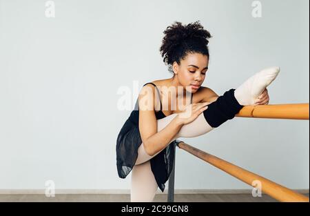 Female ballet dancer stretching her leg. Young woman preparing for a ballet class in a studio. Stock Photo
