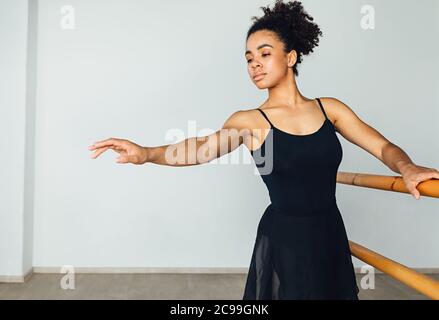 Young African American woman practicing ballet exercises holding a wooden handrail Stock Photo