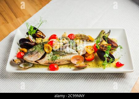 Grilled dorado fish on a white plate with cherry tomatos and mussels Stock Photo