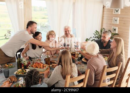Big family sitting at the table and toasting with glasses of red wine they celebrating holiday for dinner Stock Photo