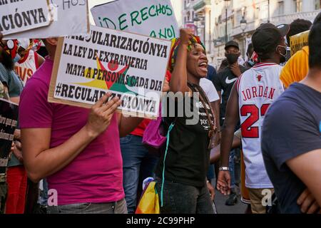 Woman in a black Regularizacion Ya T-shirt shouts beside a placard about the Ley de Extranjeria and a man in a Jordan 23 vest, Madrid, 2020 Stock Photo