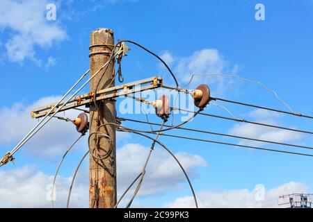 The top of an old concrete pillar with electric wires and a connected three-phase current stands against a blue cloudy sky. Stock Photo