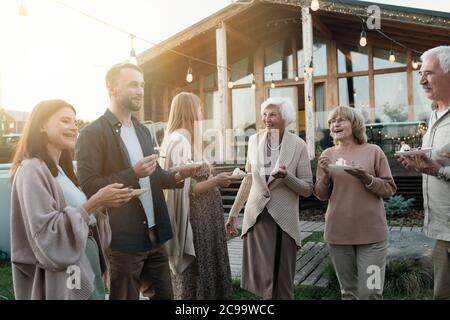 Happy big family eating cake and laughing while standing on fresh air Stock Photo