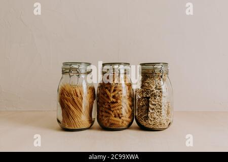 Three glass jar containers full with dried uncooked food ingredients. Rice, pasta, flour, sugar. Stock Photo
