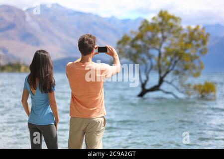 New Zealand tourists taking phone pictures of Wanaka Lone Tree at lake. People looking at view of famous touristic attraction in south island, Otago Stock Photo