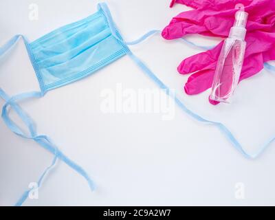 Blue protective medical face mask, a pair of pink latex gloves and a bottle of hand sanitizer on white background. Antiviral protection during covid. Stock Photo