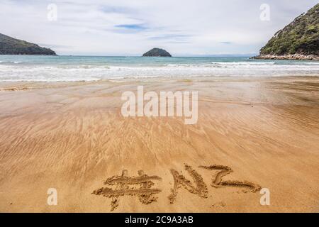 Word NZ hashtag written in sand on New Zealand beach for social media following online advertisement concept. Abel Tasman National Park beach, South Stock Photo