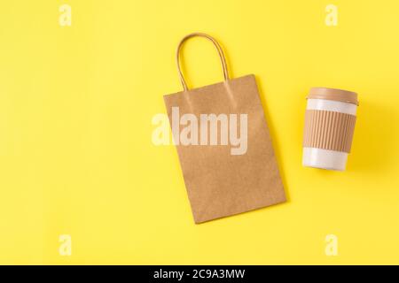 Mockup of kraft paper shopping bag with handles on yellow surface, reusable portable coffee mug for travel. Takeaway mug with spill stopper. Stock Photo