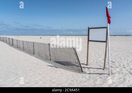 blank white sign on white sand beach with storm fencing and red flag Stock Photo
