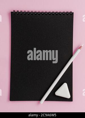 Black scetchbook mockup, white pencil and eraser on pink background. Top view, copy space Stock Photo