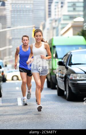 Happy couple runners exercising running outside on street. New York City active lifestyle, joggers athletes training outdoor in traffic Stock Photo