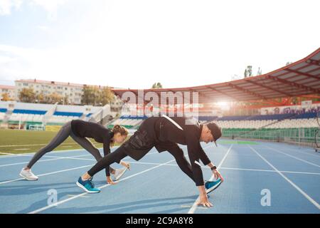 Side view photo. young sporty people doing deep lunges., active and ambitious couple training outdoorsin the evening. Stock Photo