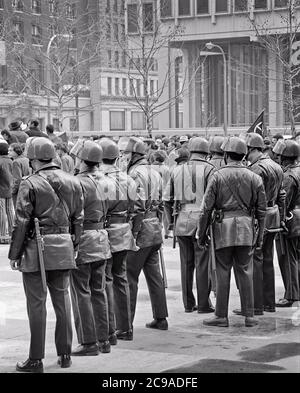 1960s 1970s LINE OF POLICE OFFICERS IN RIOT GEAR AT PROTEST RALLY DEMONSTRATION PHILADELPHIA PA USA - p7730 HAR001 HARS MASS PERSONS MALES RISK ORDER OFFICER SPECTATORS B&W GATHERING SADNESS COP FREEDOM PROTECT PROTECTION STRENGTH STRATEGY COURAGE AND EXCITEMENT EXTERIOR PA POWERFUL AT IN OF AUTHORITY DEMONSTRATION OCCUPATIONS POLITICS UNIFORMS CONCEPTUAL HELMETS OFFICERS POLICEMEN COPS IDEAS RALLY RIOT THRONG TOGETHERNESS ATTENDANCE BADGE BADGES BLACK AND WHITE HAR001 OLD FASHIONED Stock Photo