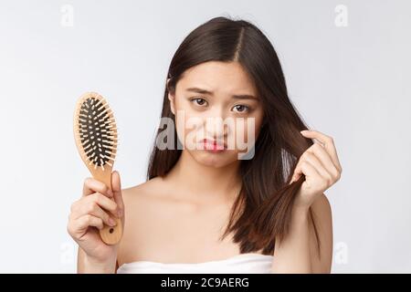 Upset stressed young Asian woman holding damaged dry hair on hands over white isolated background. Stock Photo