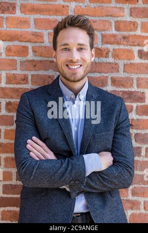 Happy smart casual businessman portrait on urban city brick wall background lifestyle portrait. Young professional man smiling confident in blazer Stock Photo