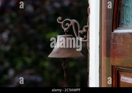 Old iron door bell hanging from the wall outside an open wooden door Stock Photo