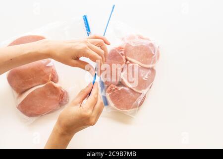 Raw boneless pork loin chops in zip lock bags. Woman packs meat in bags, close up view, white background, directly from above Stock Photo