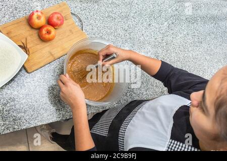 Top View of a teenage girl preparing a cake mix with a group of apples in the kitchen. Process for making apple pie Stock Photo