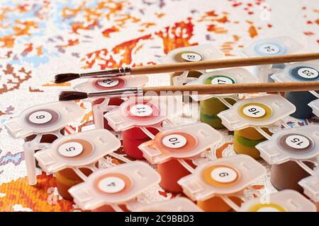 Vivid paints and brushes lay on canvas with numbers prepared for art education. Hobby and leisure activity. Background texture and art lessons