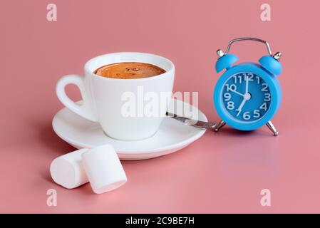 Morning cup of coffee, two marshmallows and blue alarm clock on pink background. 7 o'clock on clock face. Start of the day concept. Copy space Stock Photo