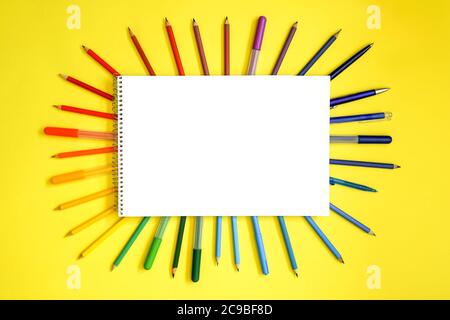 Stationery on yellow. Flat lay. Rows of tools as frame, gradient rainbow colors. Empty white blank with place for text. Stock Photo