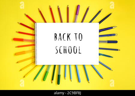 Stationery on yellow. Flat lay. Rows of tools as frame, gradient rainbow colors. White blank with text back to school. Stock Photo
