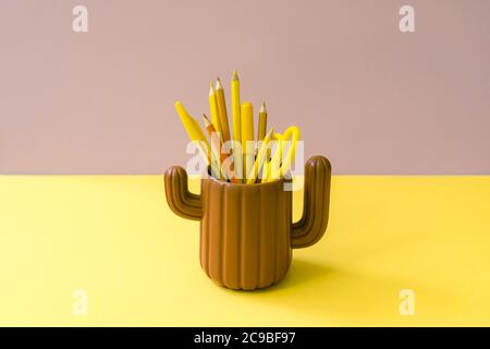 Orange yellow stationery in cactus glass on brown and yellow. Hipster minimal concept. Front view. Stock Photo