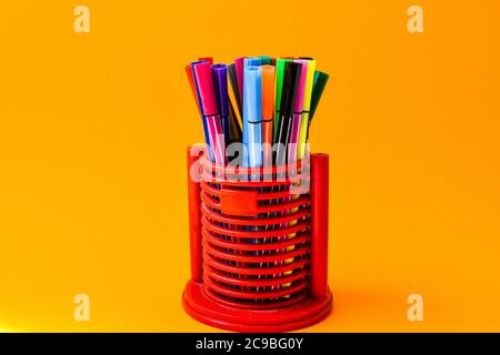 A set of multi-colored markers in an red office writing pen holder on a yellow background Stock Photo