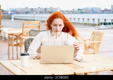 Redhead female looking at laptop in cafe outside Stock Photo