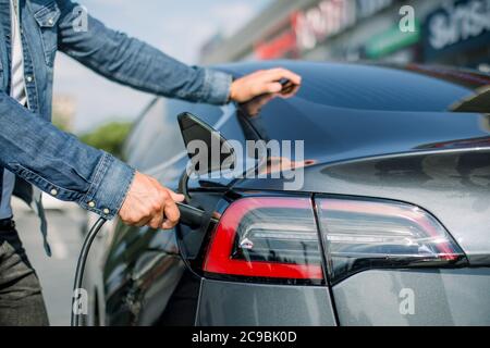 Horizontal cropped close up image of a man's hand preparing to charge an electric car at city charching station. Copy space. Eco electric car concept Stock Photo