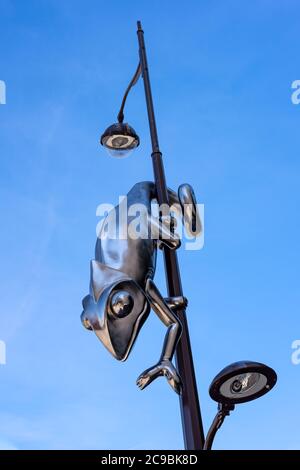 Giant stainless steel chameleon hanging from a lamp post, isolated on a deep blue sky. Stock Photo