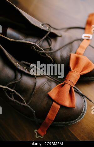 Close-up of orange groom bow tie on brown mens boots with untied laces on the parquet floor. Stock Photo