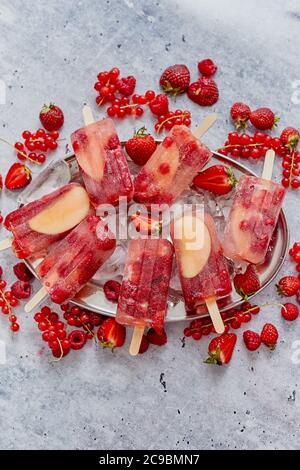 Homemade raspberry, strawberry, apple and currant popsicles on metal plate with ice assorted berries Stock Photo