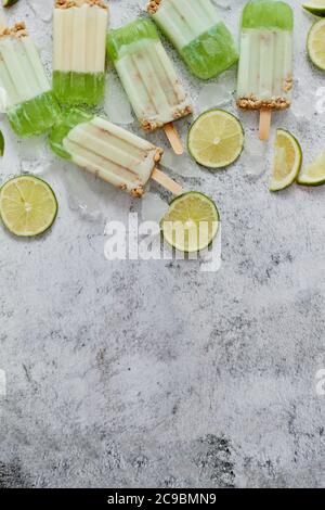 Lime and cream homemade popsicles or ice creams placed with ice cubes on gray stone backdrop Stock Photo