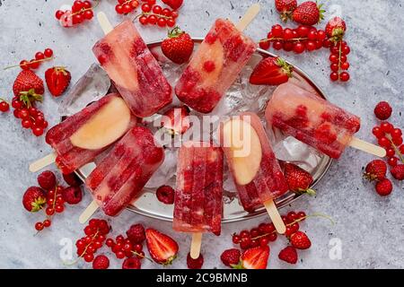 Homemade raspberry, strawberry, apple and currant popsicles on metal plate with ice assorted berries Stock Photo
