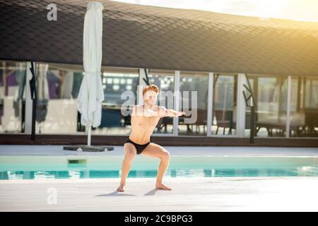 Energetic man crouching near pool on sunny morning. Stock Photo