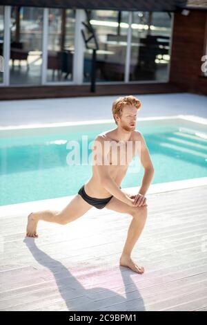 Young adult man doing warm-up near outdoor pool Stock Photo