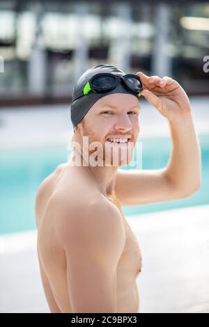 Satisfied man in swimming cap and goggles near pool Stock Photo