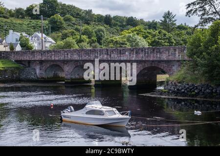 Bridge over the Glendun River on Main Street in Cushendun, County Antrim, Northern Ireland with small white pleasure boat in foreground Stock Photo