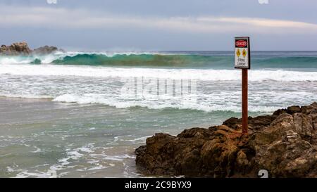 A warning sign with a big wave selectively blurred on the beach at Petrel Cove located on the Fleurieu Peninsula Victor Harbor South Australia on July Stock Photo