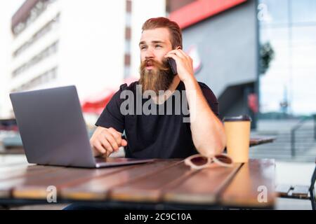 Happy male freelancer enjoying break for smartphone calling to best friend using roaming connection outdoors, cheerful bearded man making internationa Stock Photo
