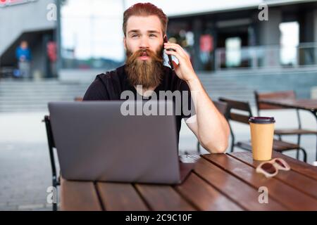 Happy male freelancer enjoying break for smartphone calling to best friend using roaming connection outdoors, cheerful bearded man making internationa Stock Photo